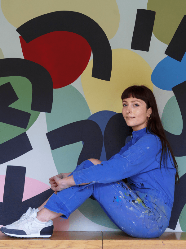 artist Caroline Dowsett sitting in front of her art work in an all denim outfit
