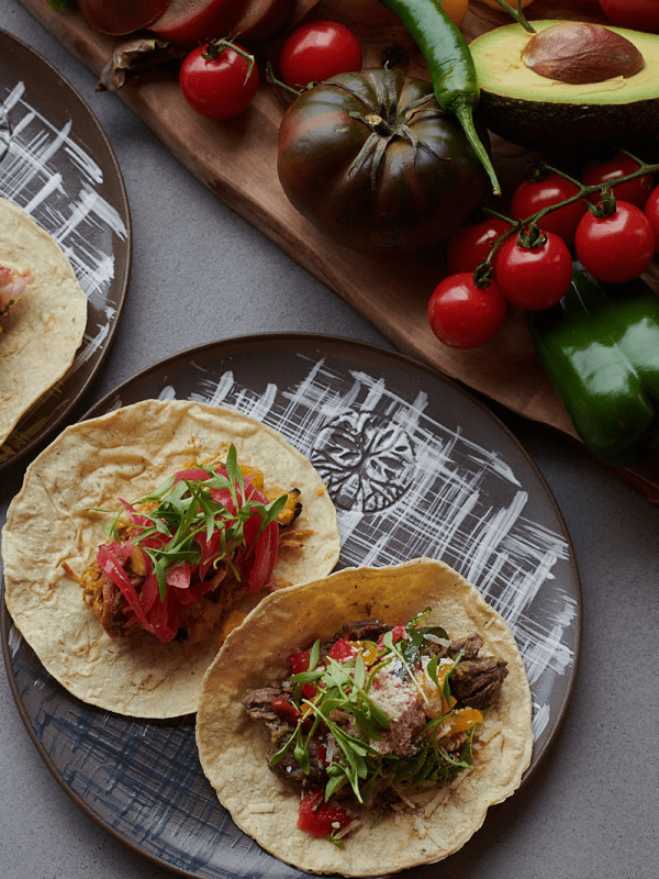Two plates of fish tacos next to an assortment of vegetables at Madera in Treehouse London.
