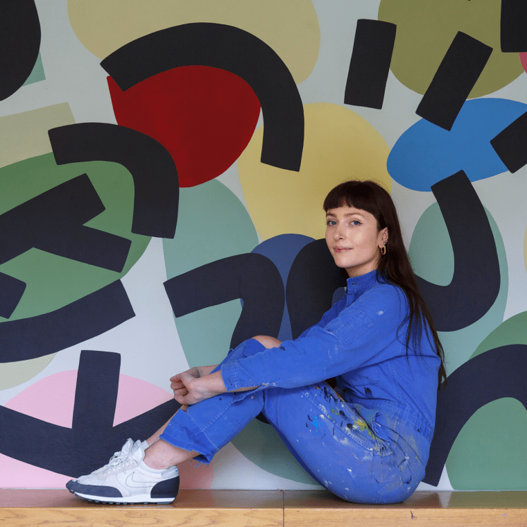 artist Caroline Dowsett sitting in front of her art work in an all denim outfit