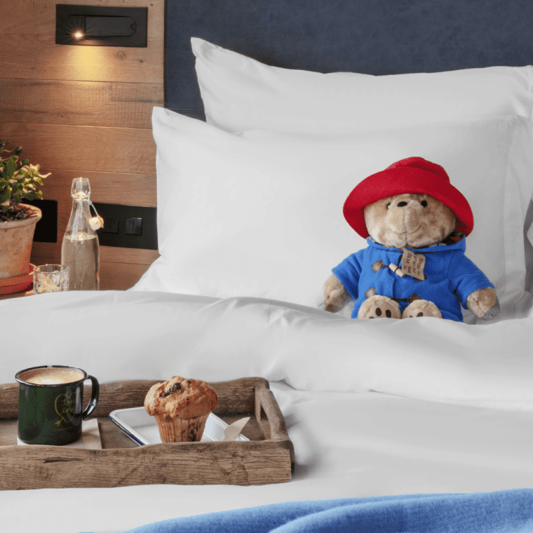 paddington bear sitting on a bed with a tray of breakfast