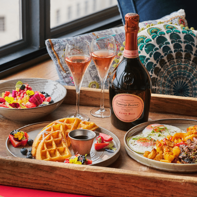 a wooden in-room dining tray with breakfast foods and two glasses of champagne