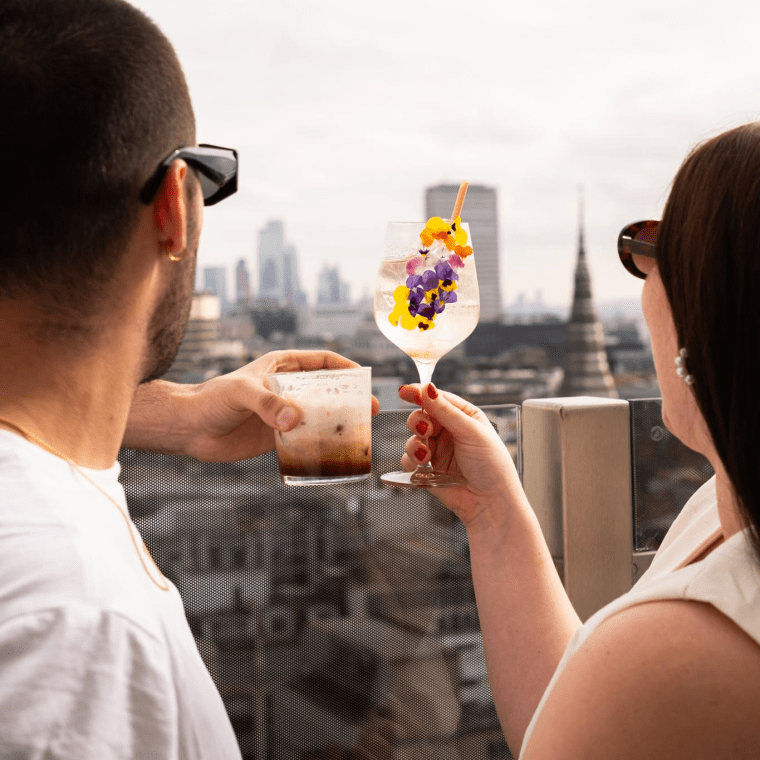 A couple raising their cocktails to the London skyline.