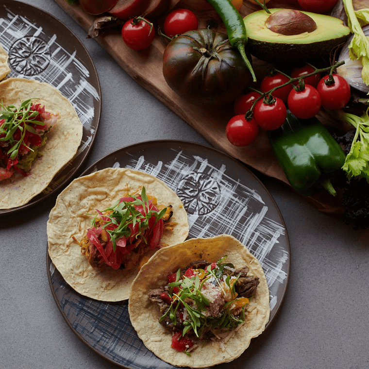 Two plates of fish tacos next to an assortment of vegetables at Madera in Treehouse London.