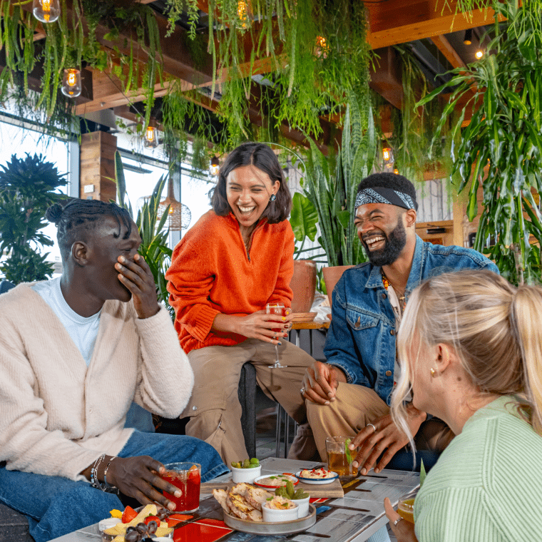 A group of friends sitting in a plant filled area of Treehouse Hotel laughing.