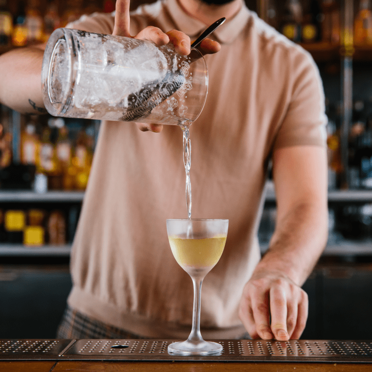 A bartender pours a drink at a bar.