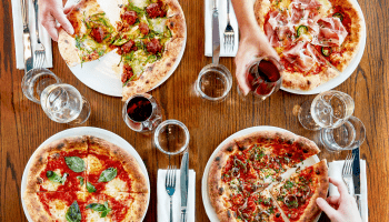 A top down view of four individual pizzas and glasses of wine at a table at Pizzeria Mozza