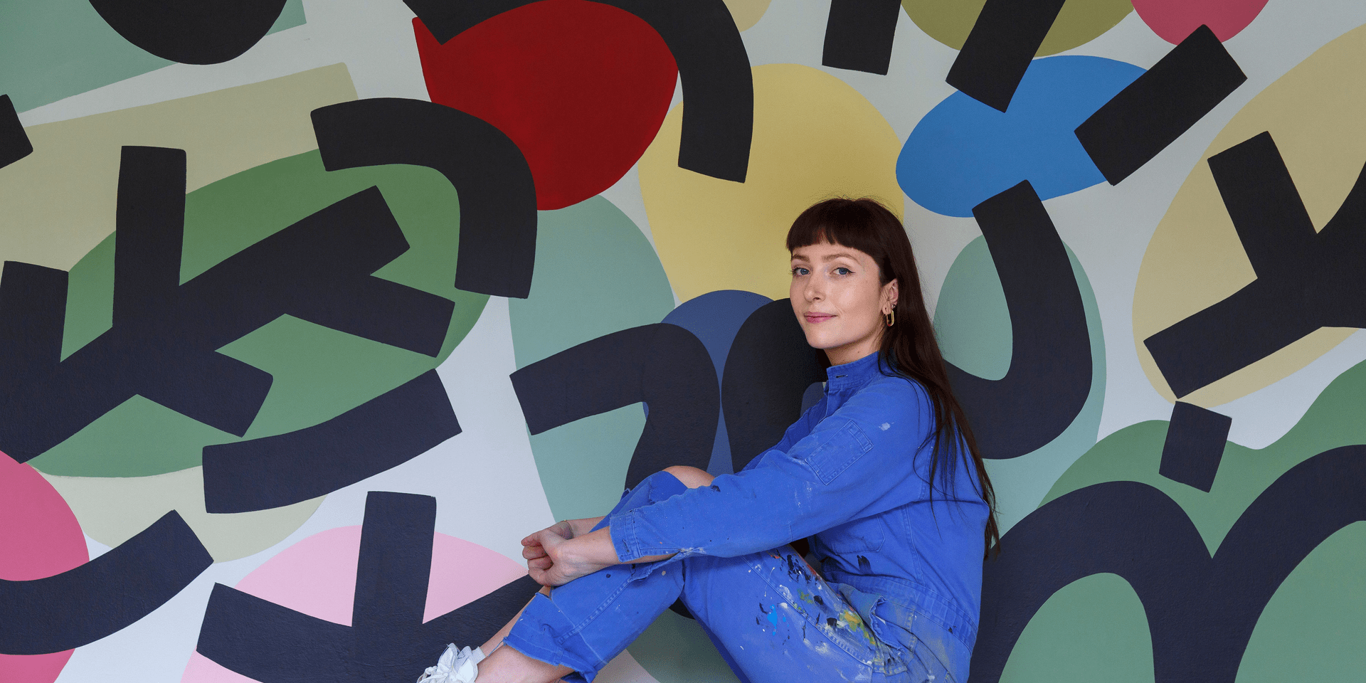 artist Caroline Dowsett sitting in front of her art work in an all denim outfit