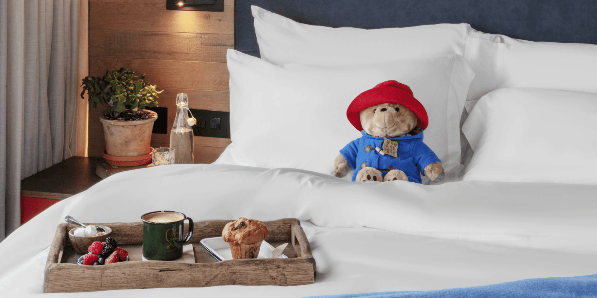 paddington bear sitting on a bed with a tray of breakfast
