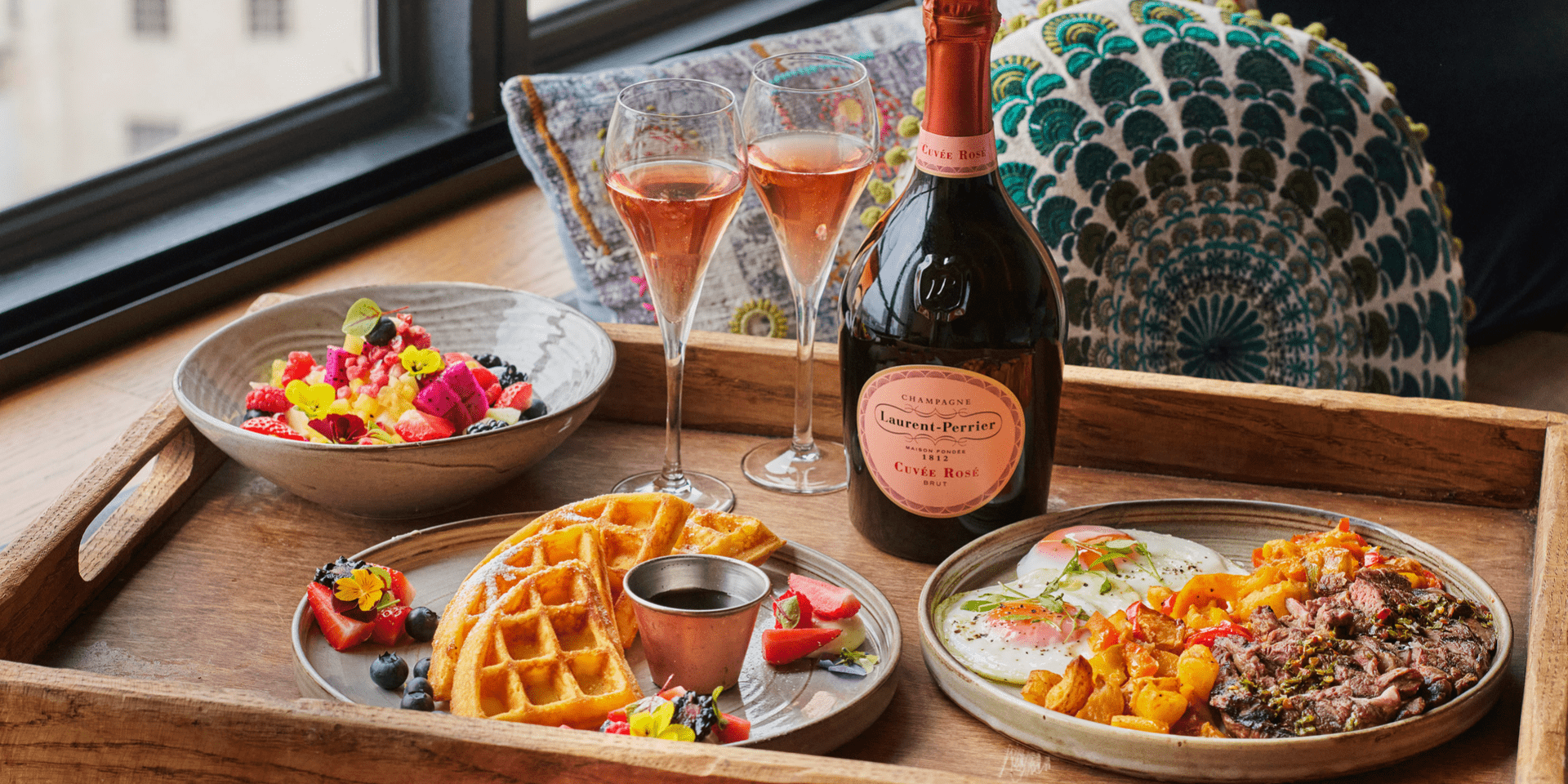 a wooden in-room dining tray with breakfast foods and two glasses of champagne
