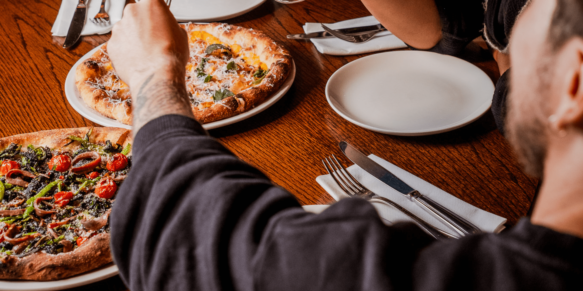 A group of people clinking wine glasses over a pizza.