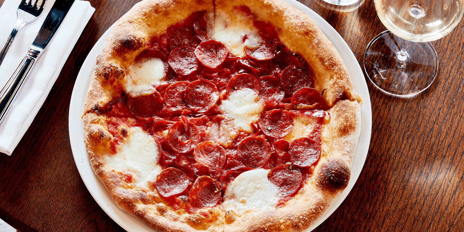 pepperoni and cheese pizza on a plate next to a class of wine