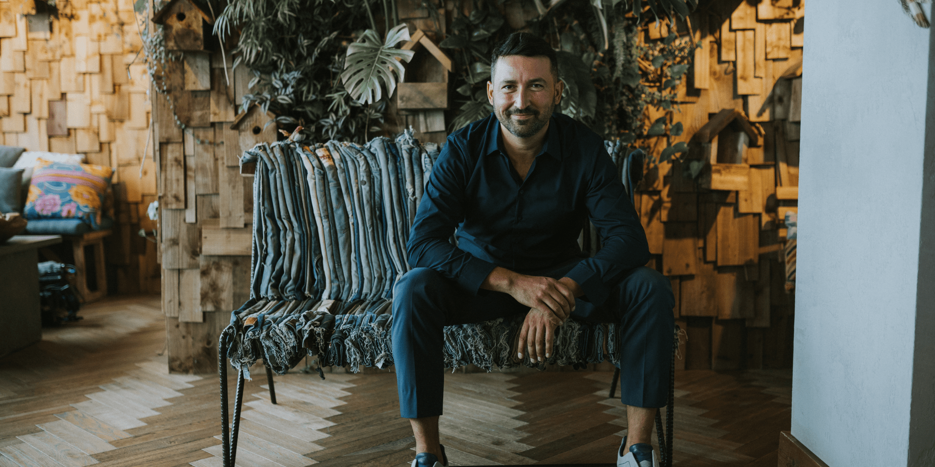 Luca Gnizio sitting on a long chair with a plant wall behind him