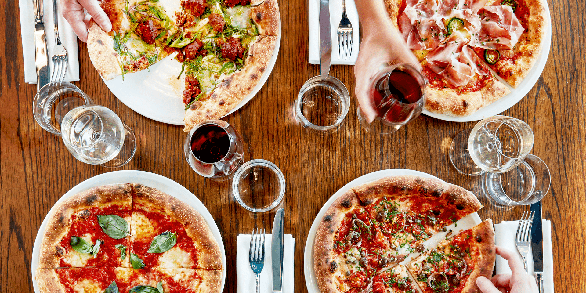 A top down view of four individual pizzas and glasses of wine at a table at Pizzeria Mozza
